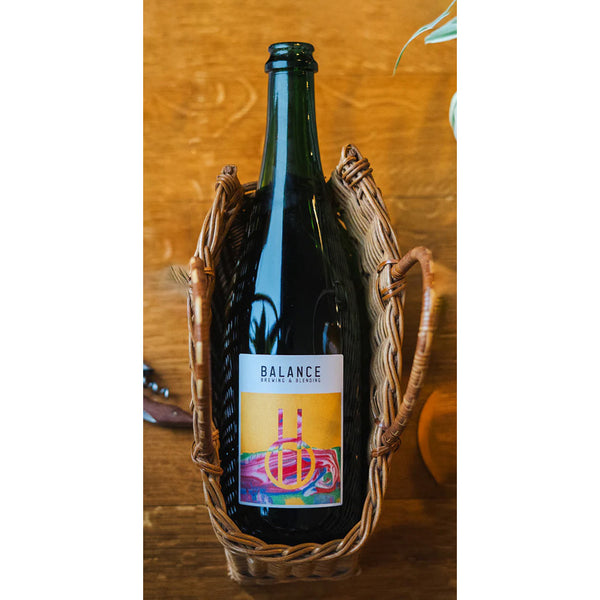 Wine bottle labeled 'Balance' in a decorative basket on a wooden surface
