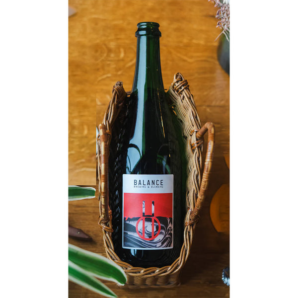 Green Beer bottle with a label in a woven holder on a wooden surface